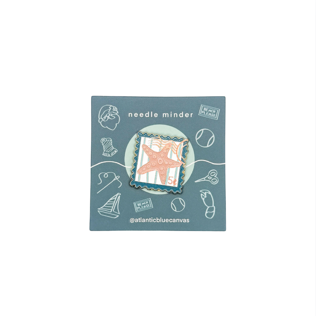 A starfish enamel pin displayed on its blue backing card, which features nautical-themed illustrations and the text 'needle minder' and '@atlanticbluecanvas'.