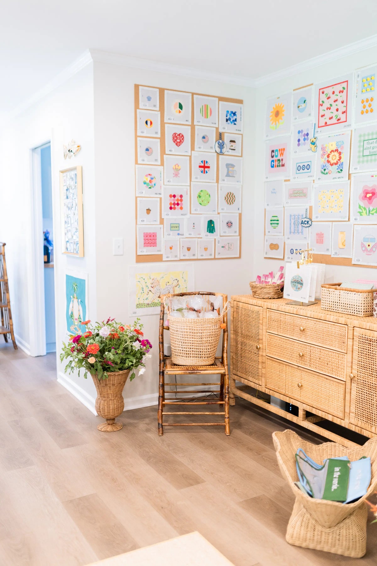 Bright Riverview Collection interior featuring a colourful needlepoint gallery wall, wicker furniture, and fresh flowers.