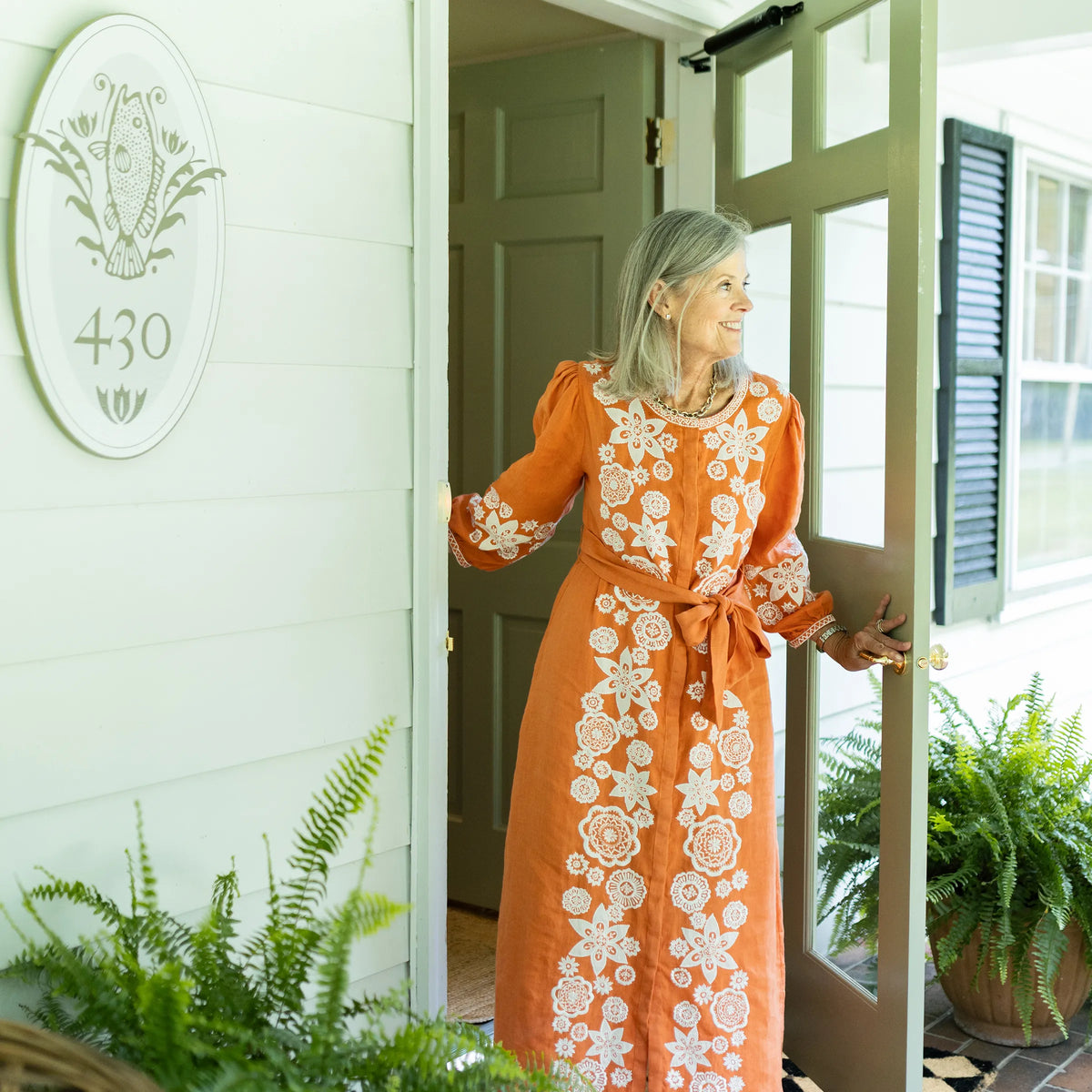 Sibby in an orange floral embroidered dress standing in the doorway of The Riverview Collection.