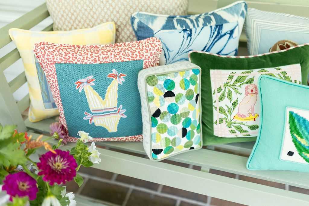 Colorful needlepoint pillows with floral and geometric designs displayed on a bench at The Riverview Collection.